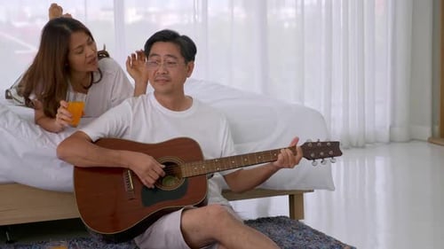 Man Plays Guitar for Wife in Bedroom