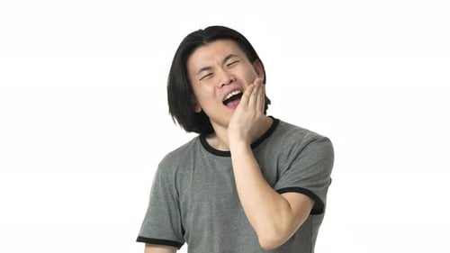 Porträt eines stirnrunzelnden chinesischen Mannes in lässigem grauem T-Shirt, der unter Zahnschmerzen leidet und den Kieferknochen berührt
