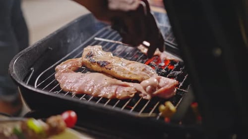 Gros plan d'un barbecue faisant griller de la viande sur un feu de cheminée avec de la fumée sur la grille du barbecue pendant la nuit noire dans le camp.