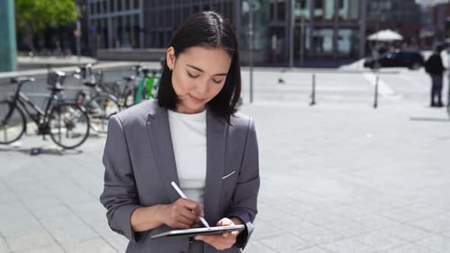 Smiling Young Asian Business Woman Using Digital Tablet on City Street