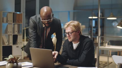 Multiethnic Businessmen Discussing Project on Laptop in Office at Night
