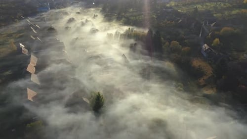 Flying Above a Remote Village Covered in Morning Haze and Mist in Early Morning Lights