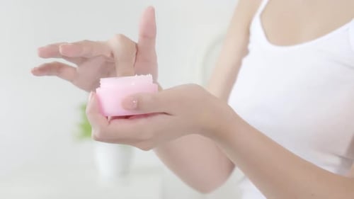 Woman Applying Cream from Pink Jar Close Up