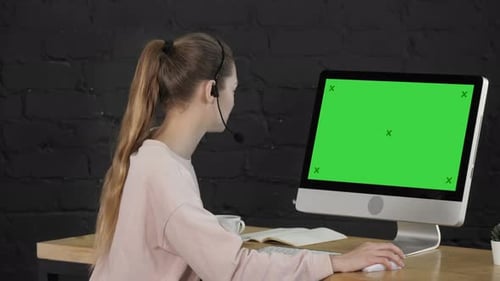 Lächelnde junge Frau mit Headset telefoniert vor dem Monitor