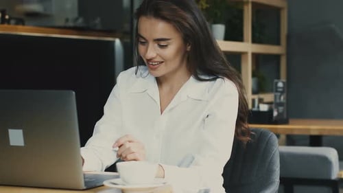 Happy Business Woman Sitting at Table in Cafe and Holding Arms Outstretched Enjoying New Achievement