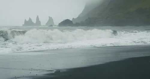 The Black Sand Beach of Reynisfjara with Waves Hitting the Shore on Foggy Rainy Stormy Day