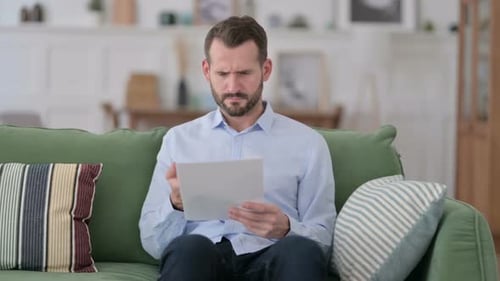 Upset Young Man Reading Documents at Home Problem
