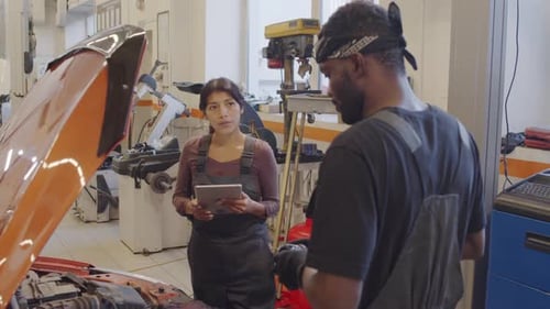 Female Mechanic Using Tablet and Talking with Colleague in Garage