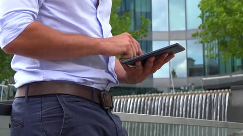 Ein Geschäftsmann arbeitet auf einem Tablet - Nahaufnahme - ein Bürogebäude im verschwommenen Hintergrund