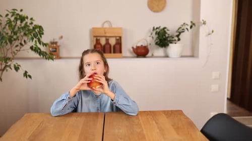 Girl Eating Red Apple at Wooden Table