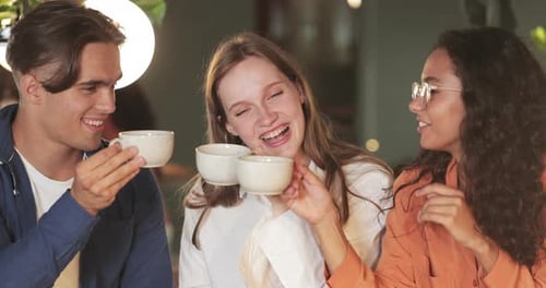 Millennial People Cheering with Cups and Laughing While Sitting in Modern Cafe. Young Smiling