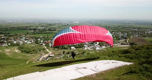 Paraglider Prepares on Hillside Above Rural Landscape