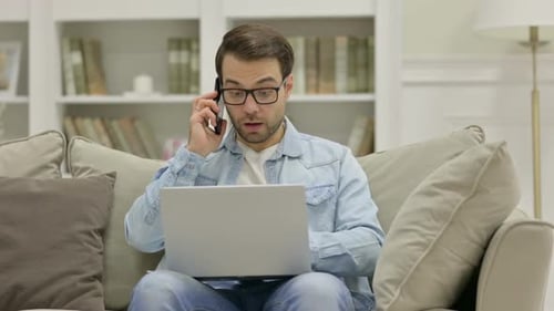 Man Working on Laptop and Talking on Phone