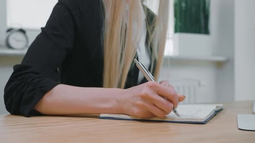Woman Writing in Notebook at Desk in Office