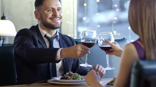 Man and Woman Clinking Wine Glasses in Restaurant