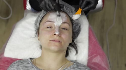 Cosmetóloga que aplica una máscara hidratante en crema con un cepillo en el rostro de