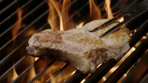 Chef turns over pork steak by a meat fork in a flame