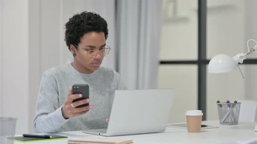 Woman Uses Phone and Laptop at Desk