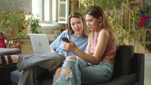Two Young Beautiful Ladies are Searching Through the Internet on the Laptop Discussing and Smiling