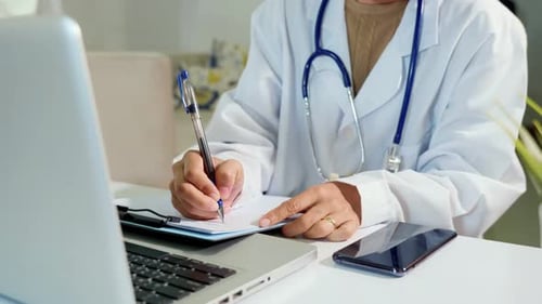 Medical Professional Writing Notes at Desk Close Up
