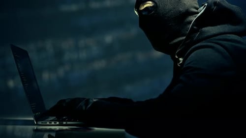 Hacker mascarado caucasiano trabalhando duro na frente de seu laptop.