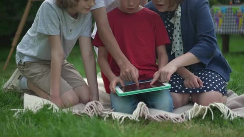 Group of Unrecognizable Children Scrolling Social Media on Tablet Having Fun on Picnic Outdoors