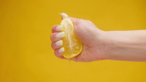 Hand Squeezing Juicy Lemon on Yellow Background