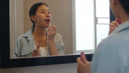 Woman Applies Lip Gloss in Bathroom Mirror