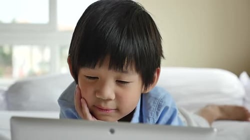 Young Child Lies on Bed Using Tablet Device