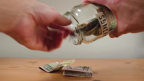Emptying Savings Jar of Paper Money on Table
