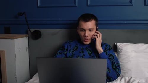 Young Adult Using Laptop and Mobile Phone in Bed