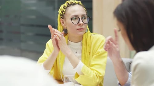 Young Woman with Yellow Dreadlocks Sits at a Desk in the Office and Discusses Working Moments with