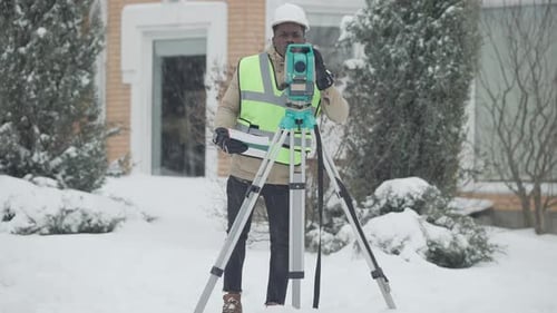 Retrato panorámico de un hombre afroamericano concentrado profesional con casco usando teodolito