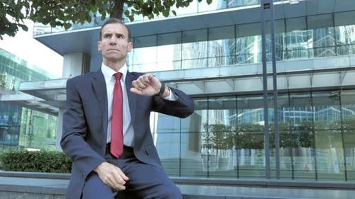 Wartender Geschäftsmann sitzt vor dem Büro und beobachtet die Zeit