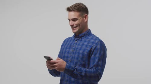Young Man Smiling Using Mobile Phone Against Plain Background