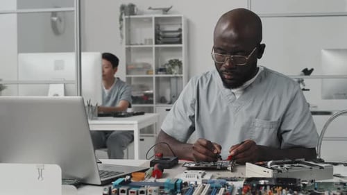 Afroamerikanischer Ingenieur testet Elektronik mit Multimeter und Laptop