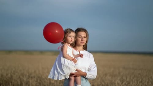 Mother with Daughter and Balloons Walking on Wheat Field