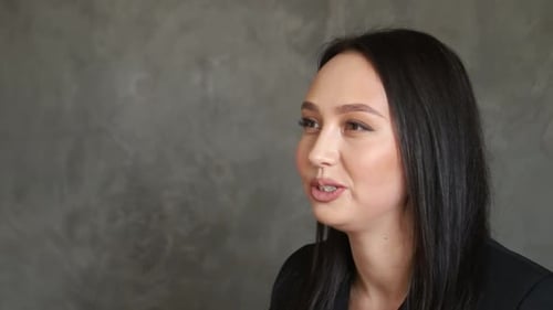 Brunette european woman looking at camera while standing in the office on gray background