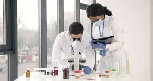 Two Scientists Using Microscope and Tablet in Lab