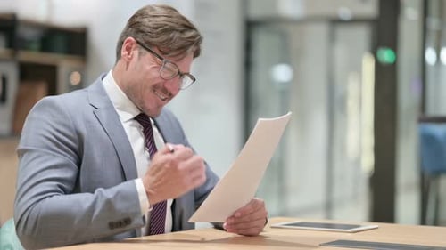 Businessman Celebrating Success on Documents in Office