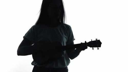 Silhouette eines Mädchens, das Ukulele in einem weißen Studio spielt