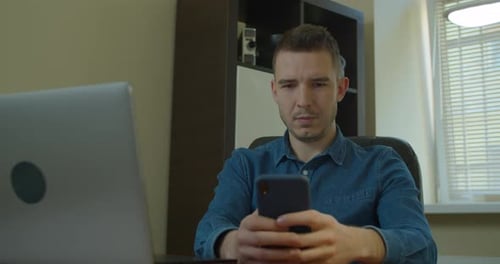 Man Using Smartphone at Desk with Laptop
