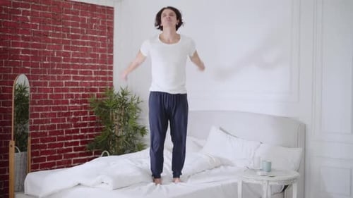 Young Adult Jumps on Bed in Bedroom