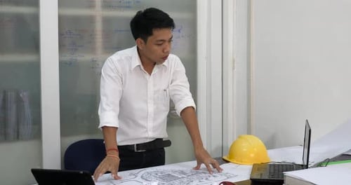 Engineer Reviews Blueprints and Plans at Desk