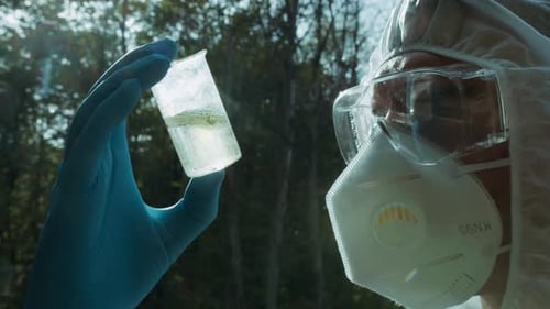 Chemist in Ppe Looking at Flask with Solution Water Analysis From Swamp Wearing Protective Suit and