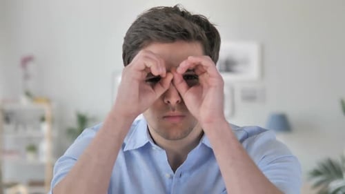 Young Man Looking Through Binoculars Made With Hands