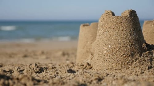 Shallow DOF of castles made of sand on the beach with ocean waves in background slow-mo 1080p HD vid