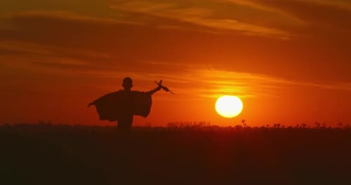 A Boy Is Running Across a Field with a Plane in His Hand. Beautiful Sunset.