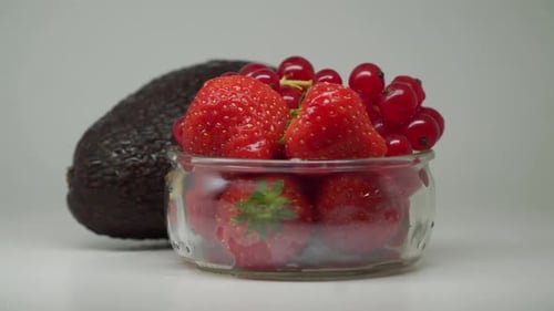 Ripe Avocado, Strawberries And Red Currants In A Clear Glass Bowl Rotating- Close Up Shot
