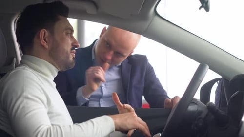 Professional Salesman Smiling Showing a New Car at the Dealership to His Male Customer